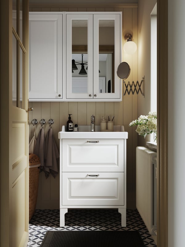 Un baño con muebles de baño blancos IKEA y sobre el lavamanos un mueble con espejo.