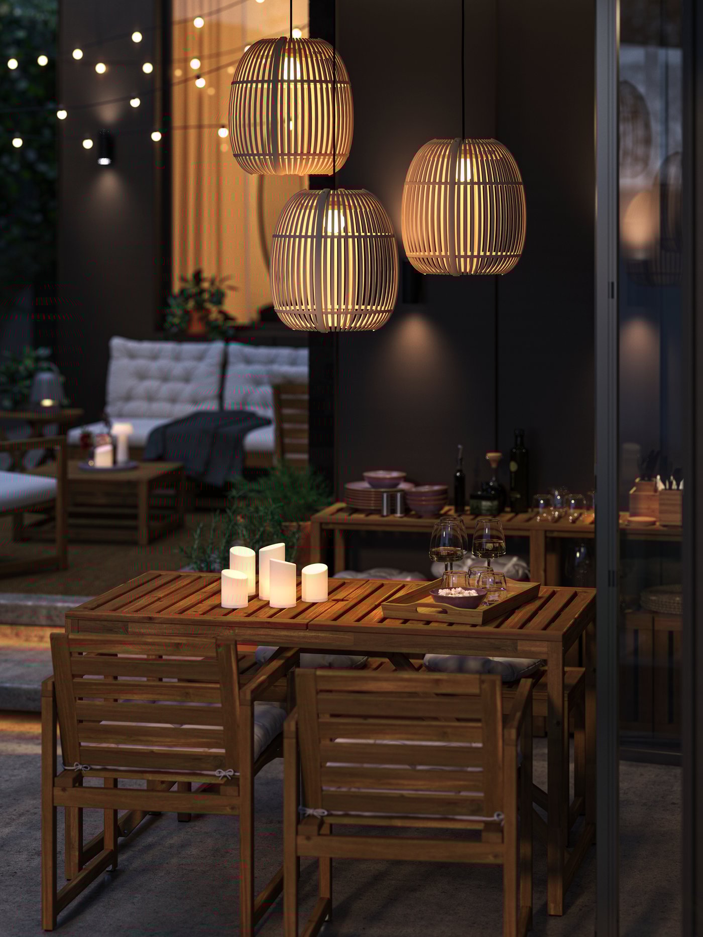 Ein Essbereich auf der Terrasse in der Abenddämmerung mit drei beleuchteten SOLVINDEN Pendelleuchten über einem NÄMMARÖ Tisch für den Aussenbereich mit LED-Kerzen und Stühlen.