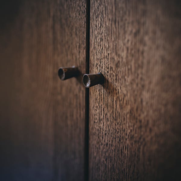 A close-up of the knobs on the doors of a brown stained oak veneer TONSTAD cabinet with doors.