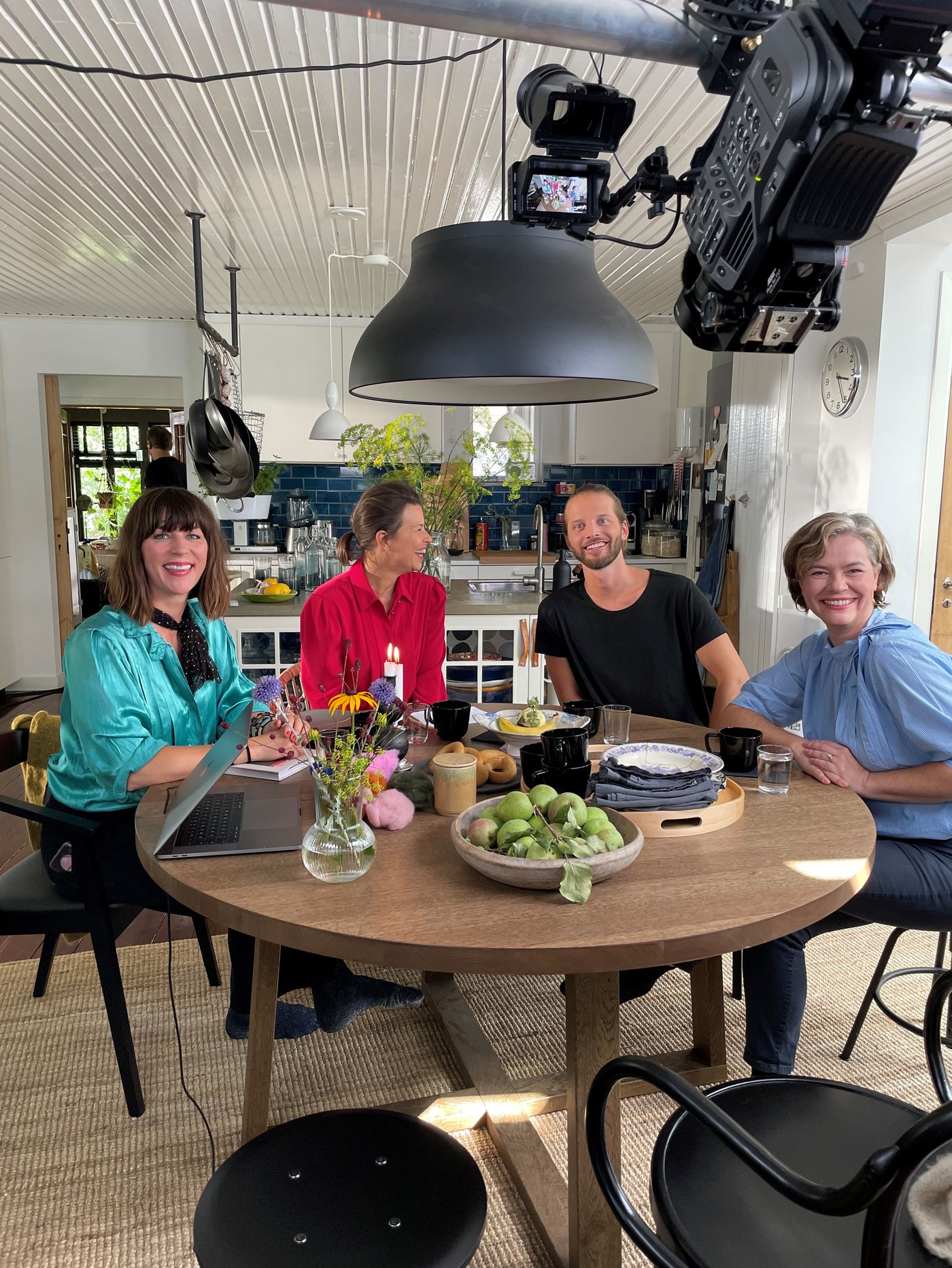 Dve žene i dva muškarca sede za trpezarijskim stolom i gledaju u kameru tokom snimanja.