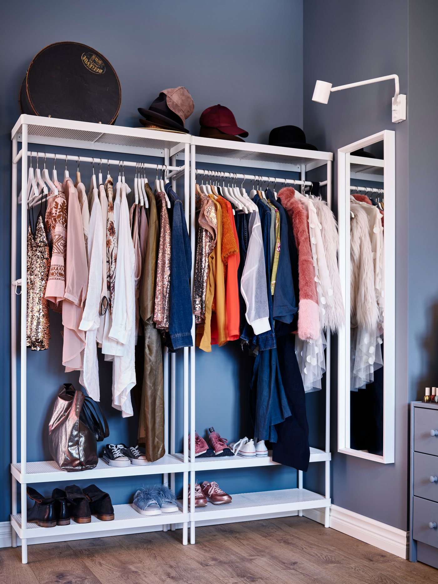 Two side-by-side, white-coated steel MACKAPÄR coat racks with shoe shelves on a blue wall next to a mirror and a wall lamp.