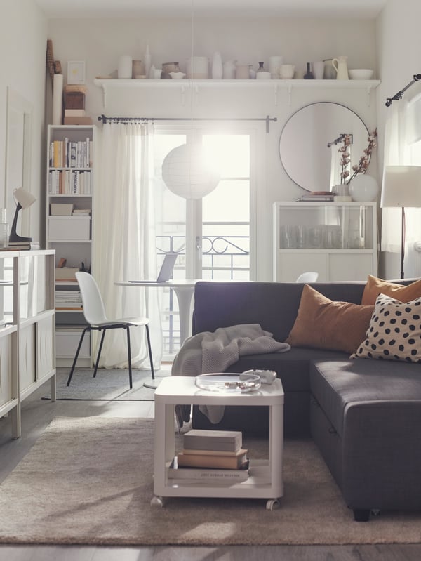 The sun shines in through the French doors of a light, modern living room centred around a dark-grey FRIHETEN sofa-bed.