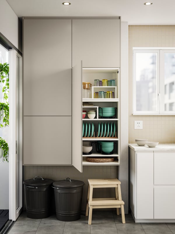 A kitchen with HAVSTORP fronts, one door is opened, revealing neatly organised plates, bowls, and glassware on the shelves.