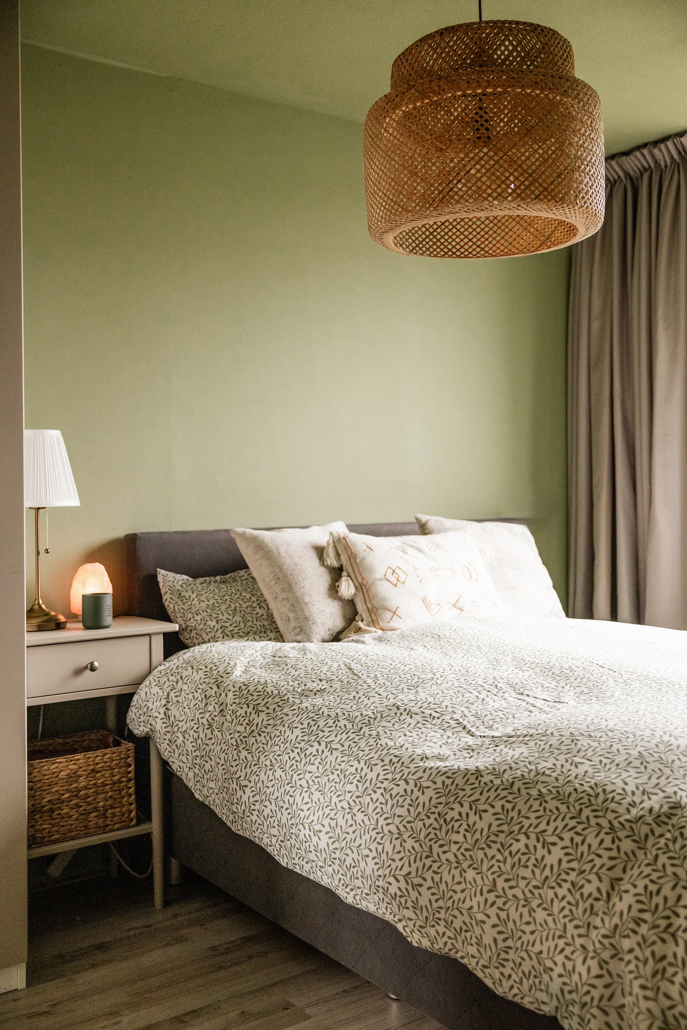 Slaapkamer met zachtgroene muren. Naast het bed staat een BLÄSTÅSEN nachtkastje, boven het bed hangt een rieten lamp.