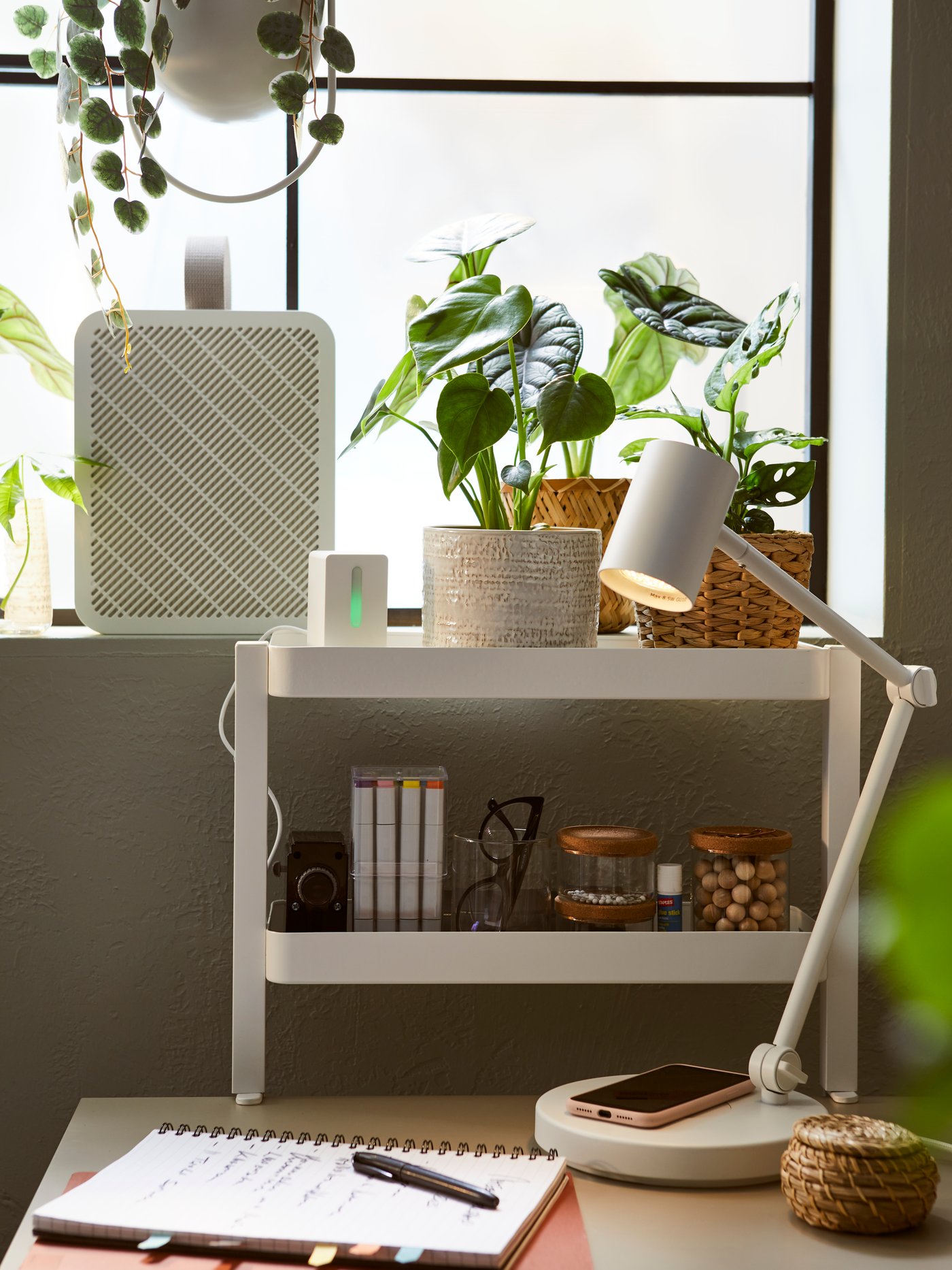 Range-tout de bureau VATTENKAR et lampe de bureau posée sur une table devant une fenêtre surmontée de plantes.