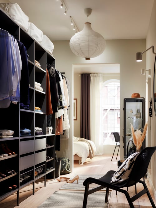 A big, dark grey AURDAL wardrobe combination is on a hallway wall leading into a bedroom. It has drawers, rails and shelves.