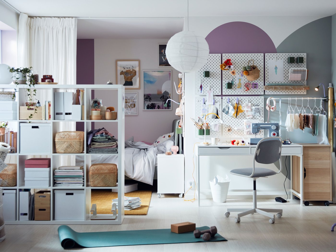 Una habitació de colors lluminosa amb taulers perforats damunt d'un escriptori ALEX, cortines i una prestatgeria KALLAX que separa una zona amb un llit.