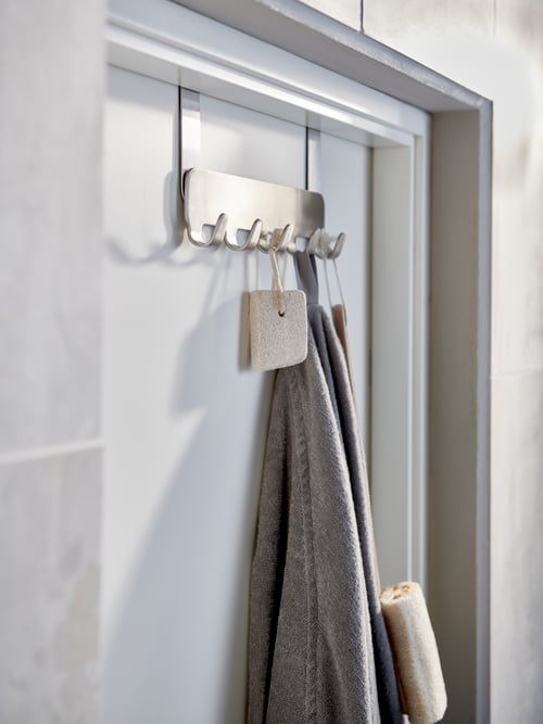 A towel and shower accessories hang from a BROGRUND hanger for door in stainless steel.