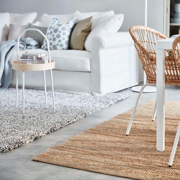 Ein Hochflor Teppich vor einem Sofa und ein Kurzflor Jute Teppich unter einem angrenzenden Essbereich.