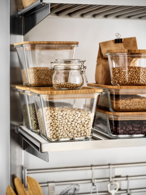 Several food containers in clear glass with bamboo lids filled with various dry foods standing on a shelf.