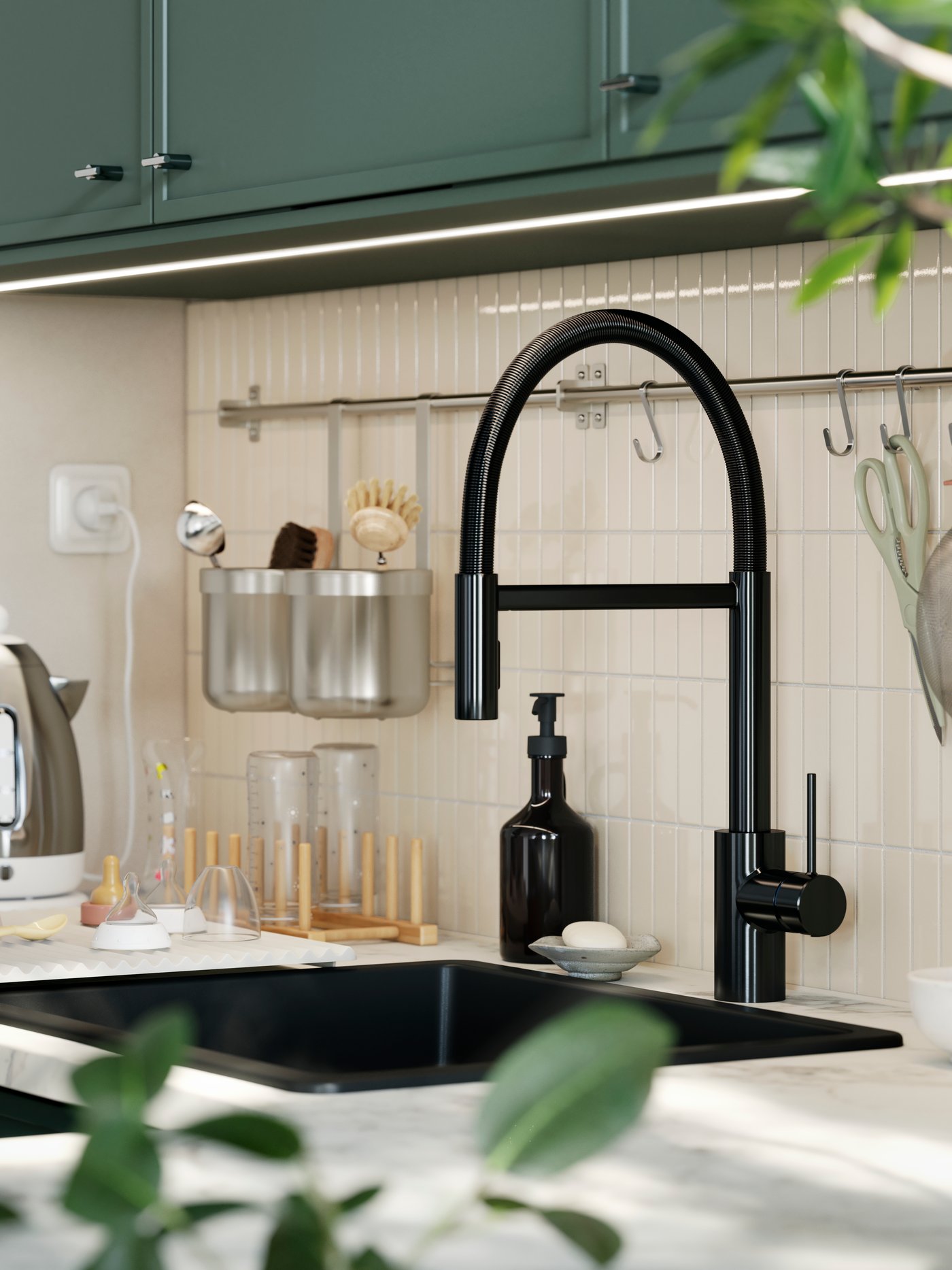 A SALLSJÖN kitchen mixer tap with a gooseneck design is mounted in a kitchen with a tiled wall and grey-green kitchen doors.