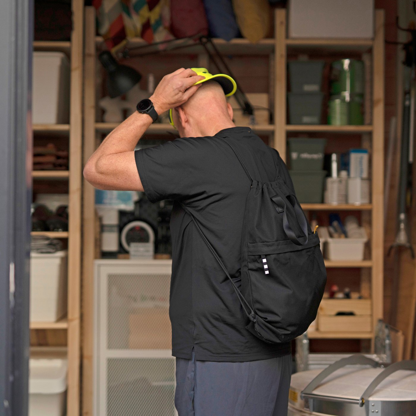 A man dressed in sports clothes and carrying a VÄRLDENS gym bag is putting a cap on his head.