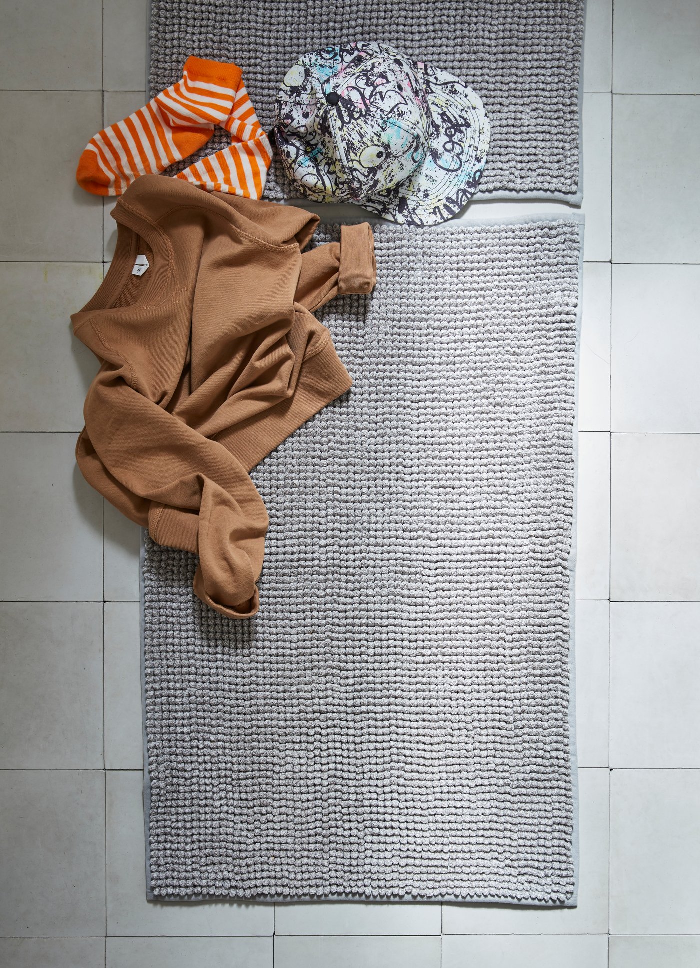 Dos pisos de baño IKEA, sobre ellos una polera, un par de calcetines y un sombrero.
