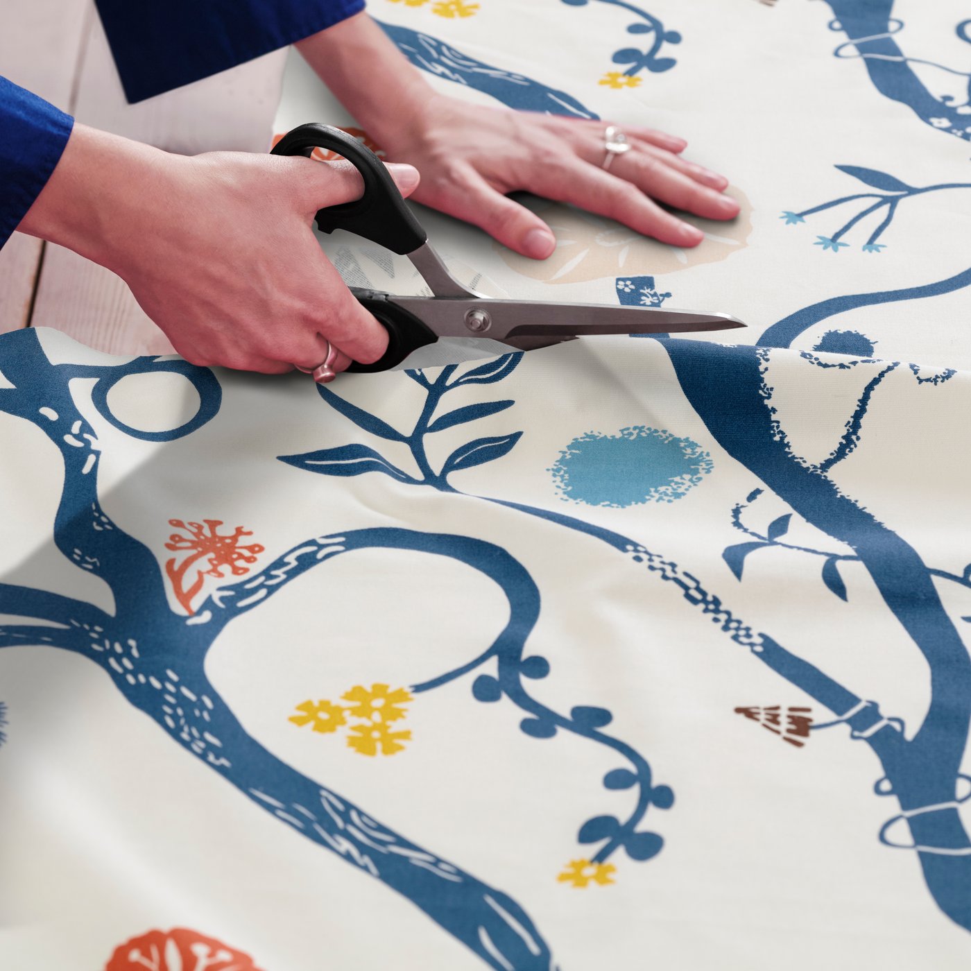 Una persona sta tagliando con delle forbici del tessuto REVFINGERÖRT bianco con motivi botanici e multicolore.