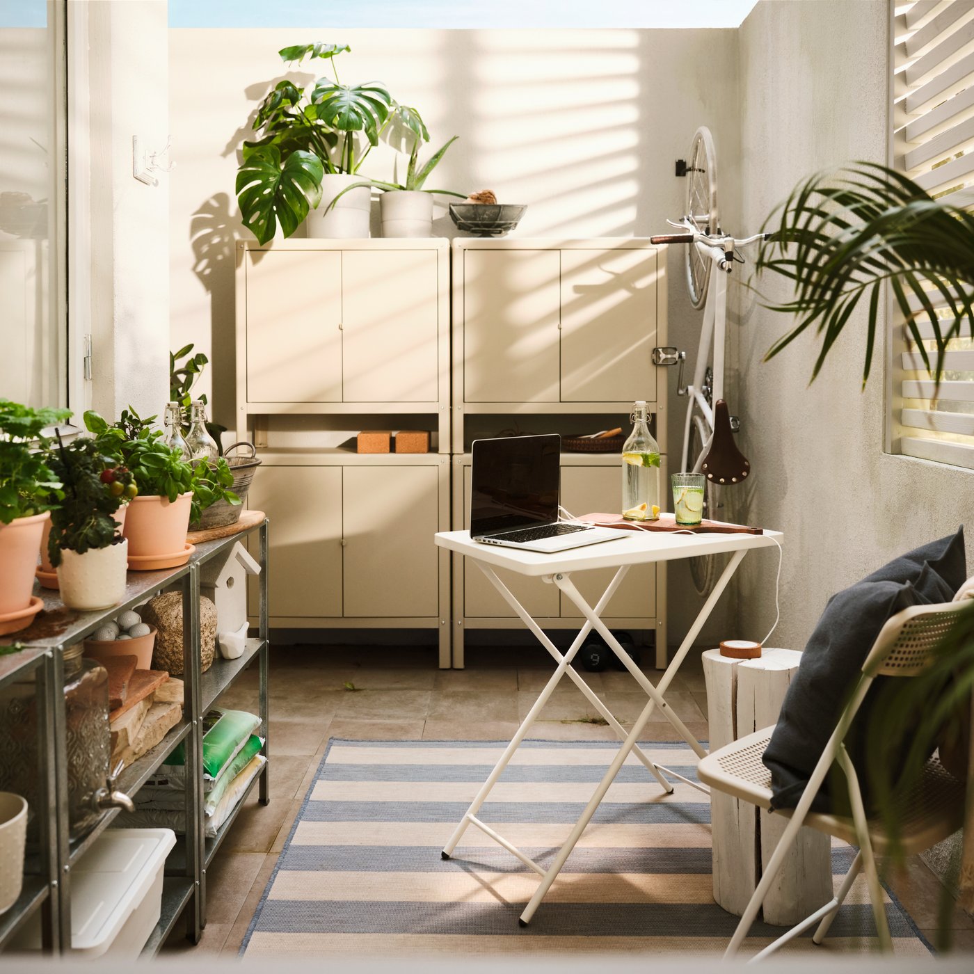 A big, beige in/outdoor KOLBJÖRN cabinet, made of two stacked cabinets on top of side-by-side cabinets, is on a balcony wall.
