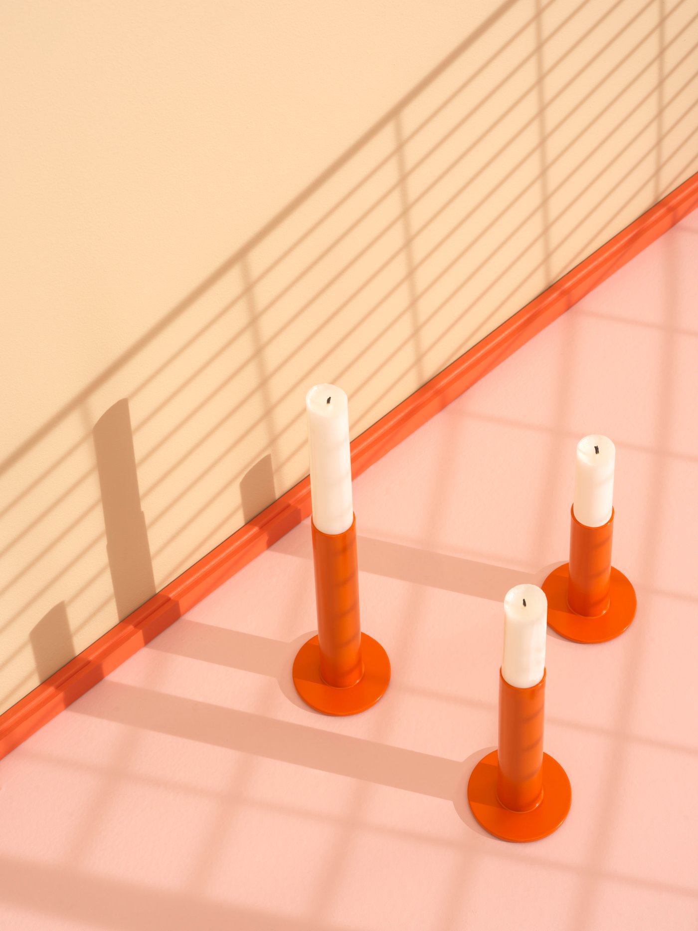 Orangene Kerzenhalter mit weißen Kerzen darin.