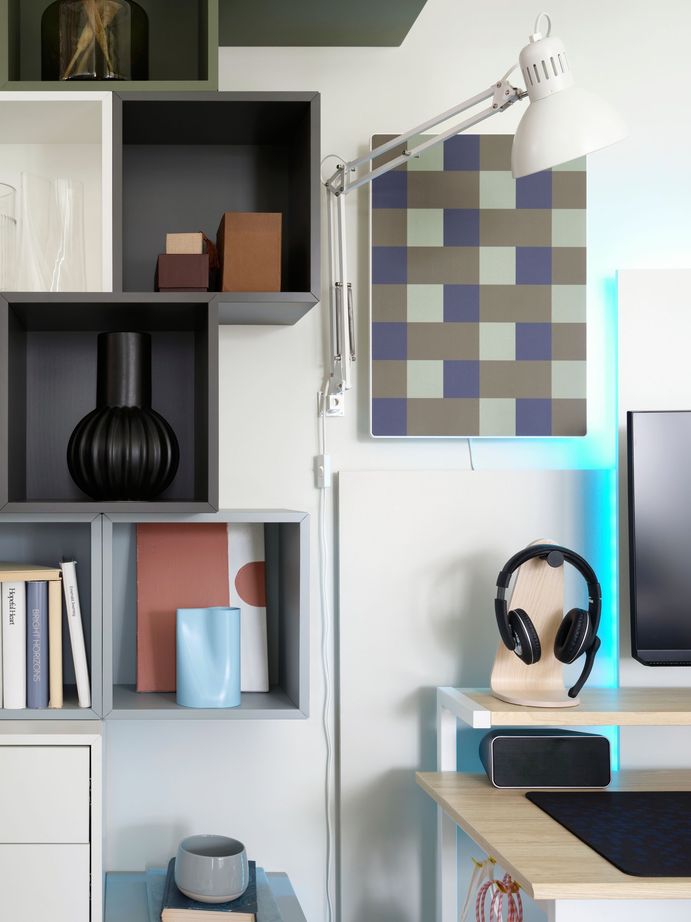 A SYMFONISK picture frame with WiFi speaker in a blue-green checkered motif hangs on a wall above a desk, by storage cubes.