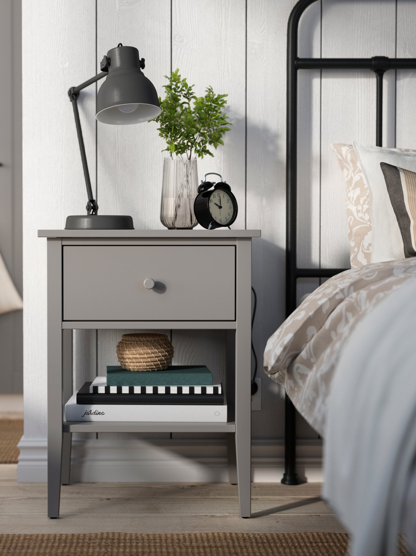 A GREY GULLABERG bedside table with a reading lamp and decoration on top.