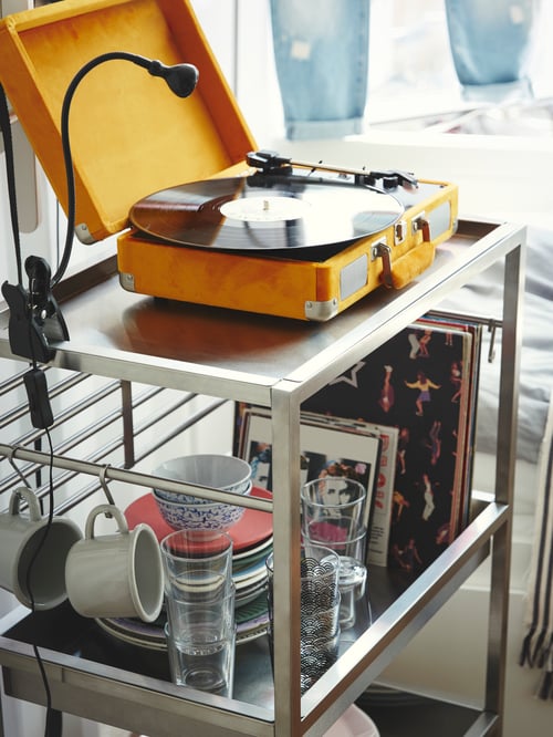KUNGSFORS trolley with yellow turntable and spot light on top shelf, and records and crockery on the shelf below.