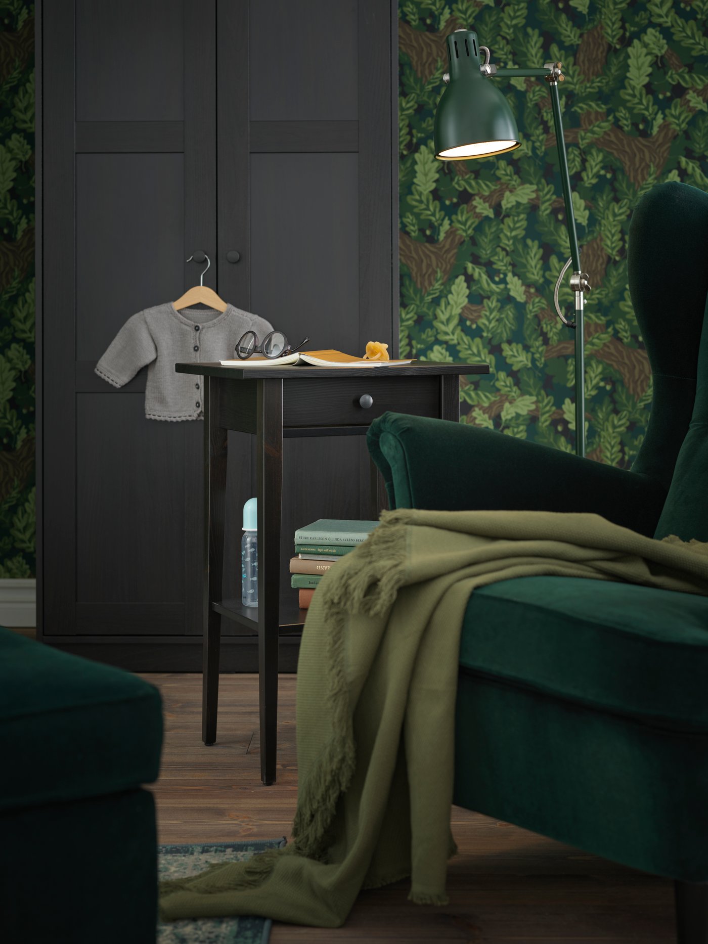 Egy STRANDMON füles fotel, egy ARÖD álló- és olvasólámpa és egy HEMNES éjjeliszekrény áll egy RAKKESTAD szekrény előtt.