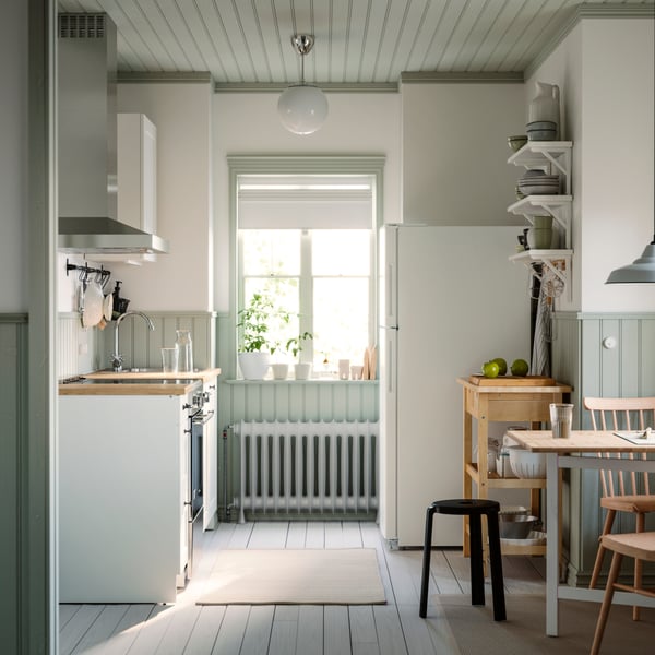 A small and bright kitchen with a window has white KNOXHULT cabinets, a dining table, and a rug on the floor.