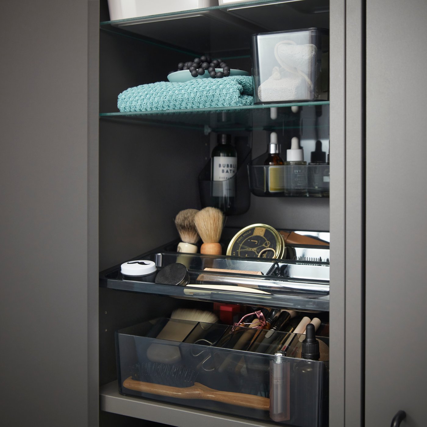 Close-up inside a dark grey HAVBÄCK high cabinet with door, displaying neatly arranged toiletries and grooming items.
