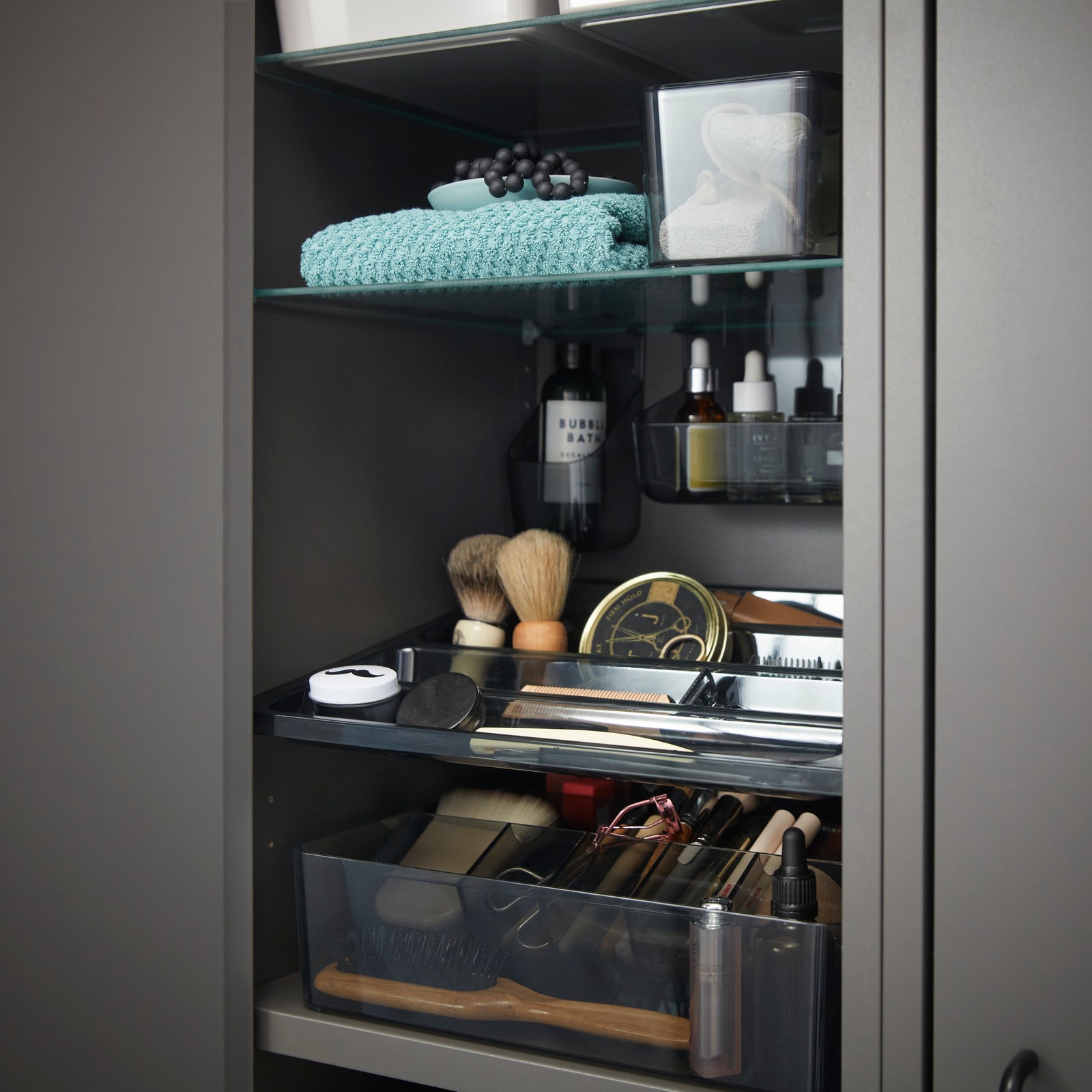 Close-up inside a dark grey HAVBÄCK high cabinet with door, displaying neatly arranged toiletries and grooming items.