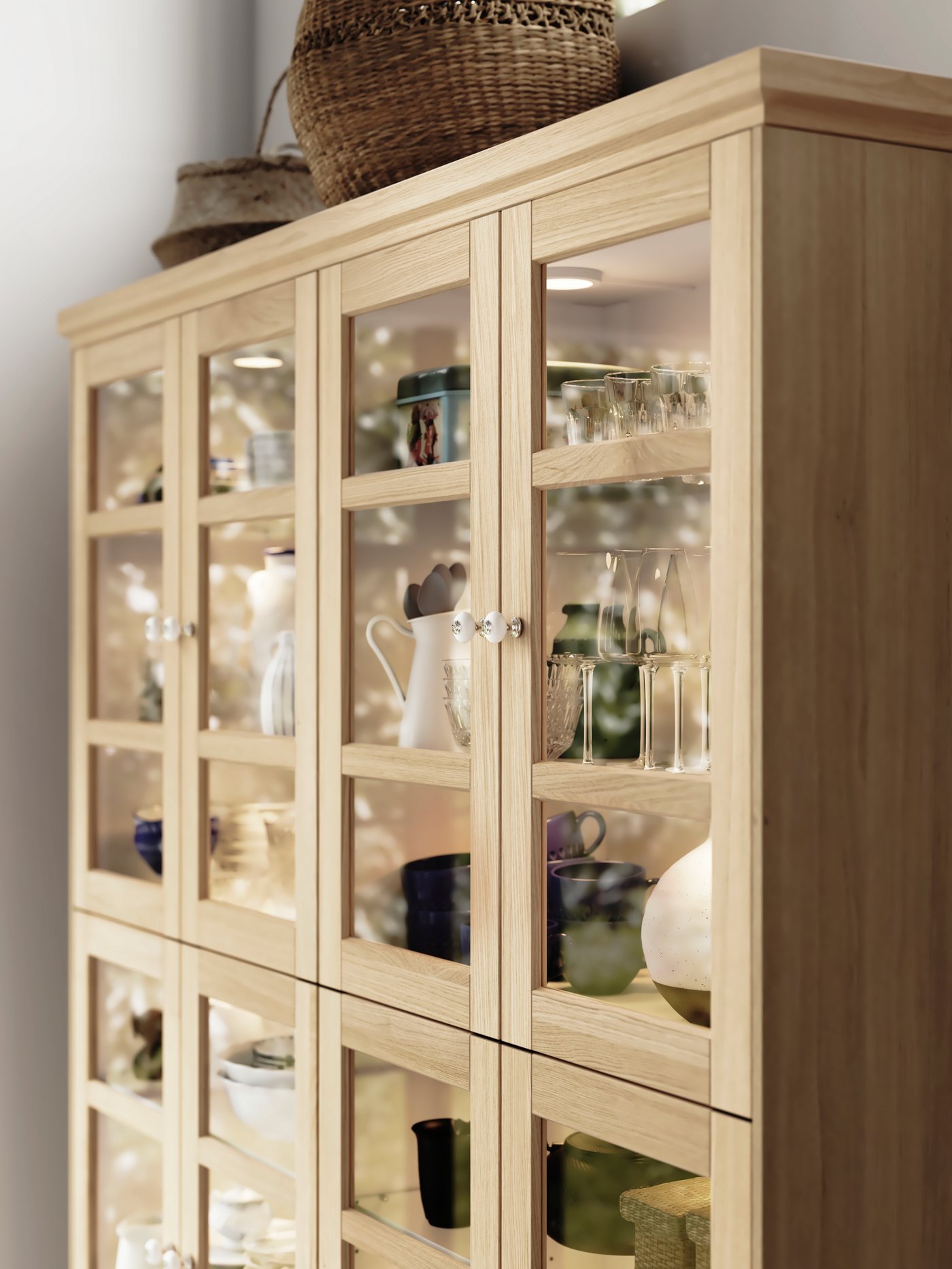 A side view of a glass-door cabinet with FORSBACKA fronts in oak veneer filled with plates, cups and other tableware.