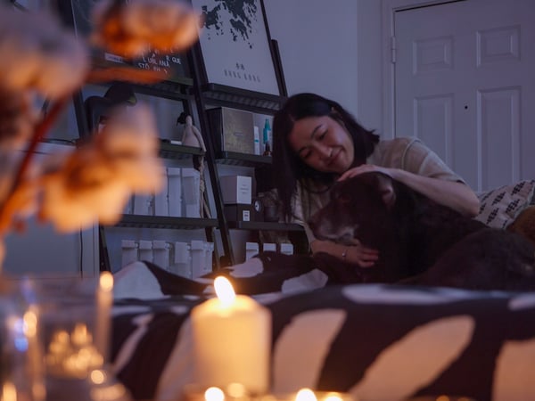 A woman and a dog relax in front of a table full of lit candles.