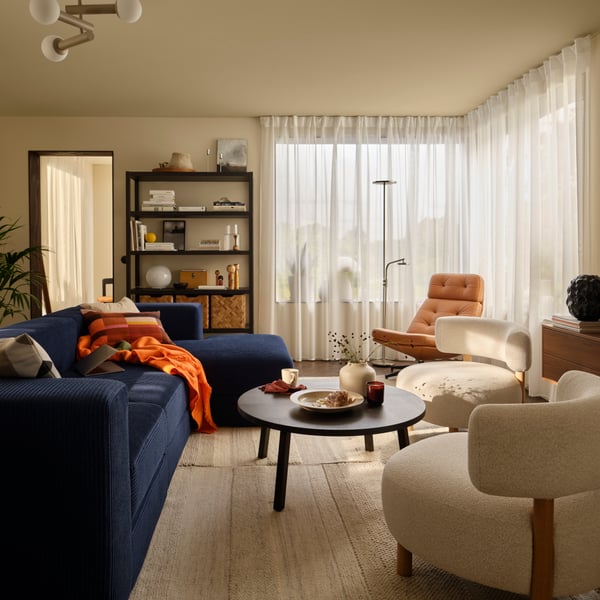 A living room with a dark-blue JÄTTEBO four-seat sofa with chaise longue next to STOCKHOLM 2025 armchairs and coffee table.