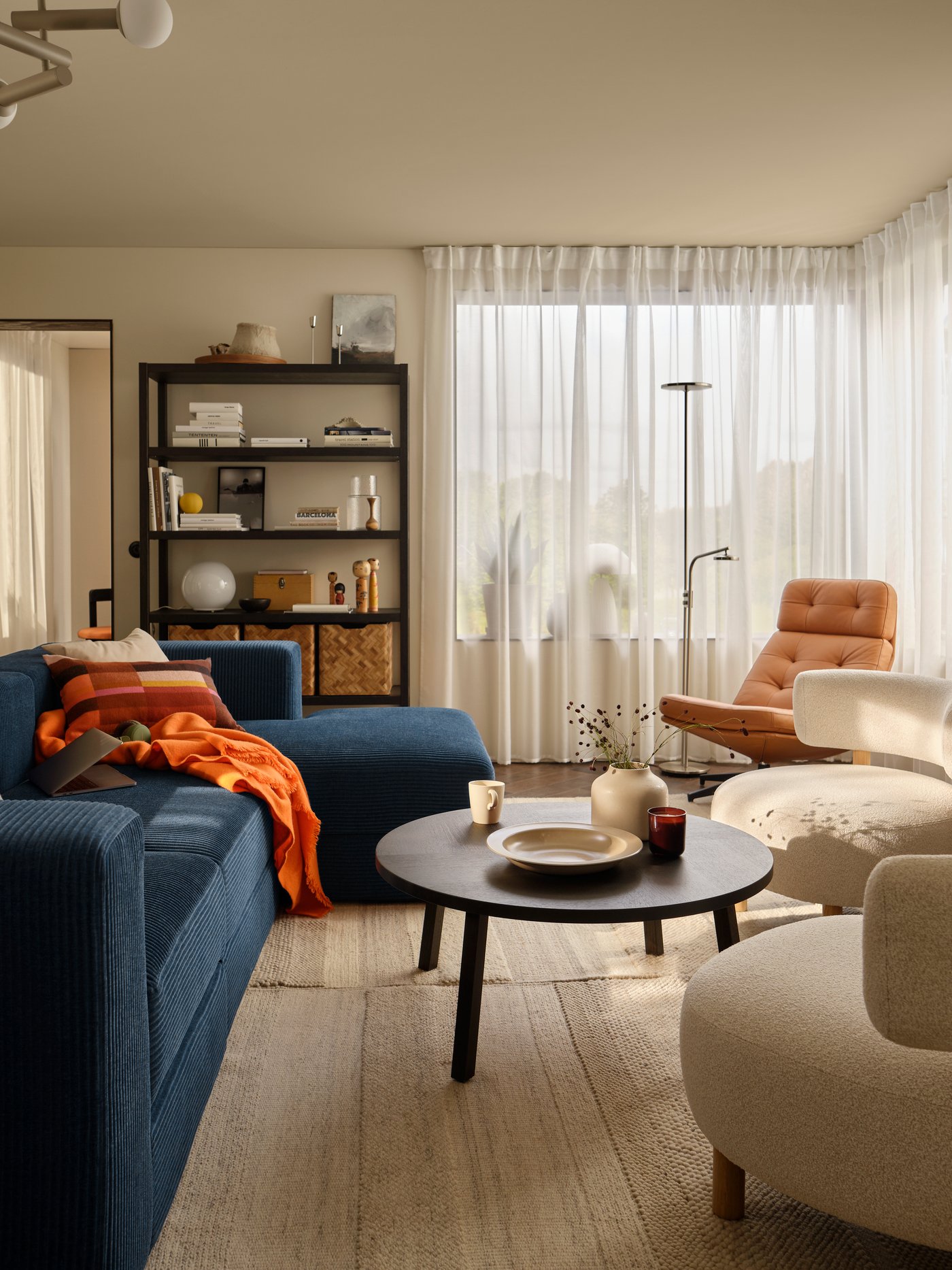 A living room with a dark-blue JÄTTEBO four-seat sofa with chaise longue next to STOCKHOLM 2025 armchairs and coffee table.