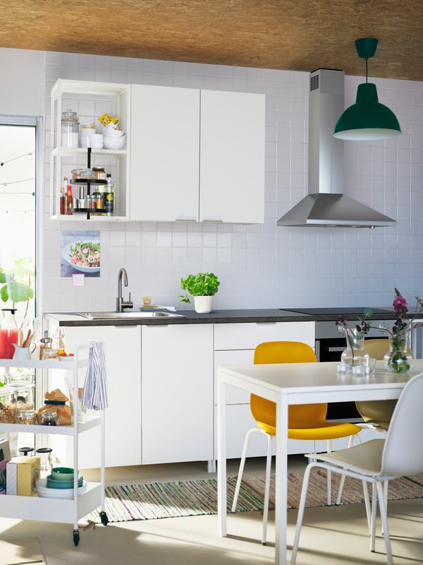 A kitchen with white ENHET cabinets, a white MELLTORP table, different-colour LEIFARNE chairs, and a white NISSAFORS trolley.