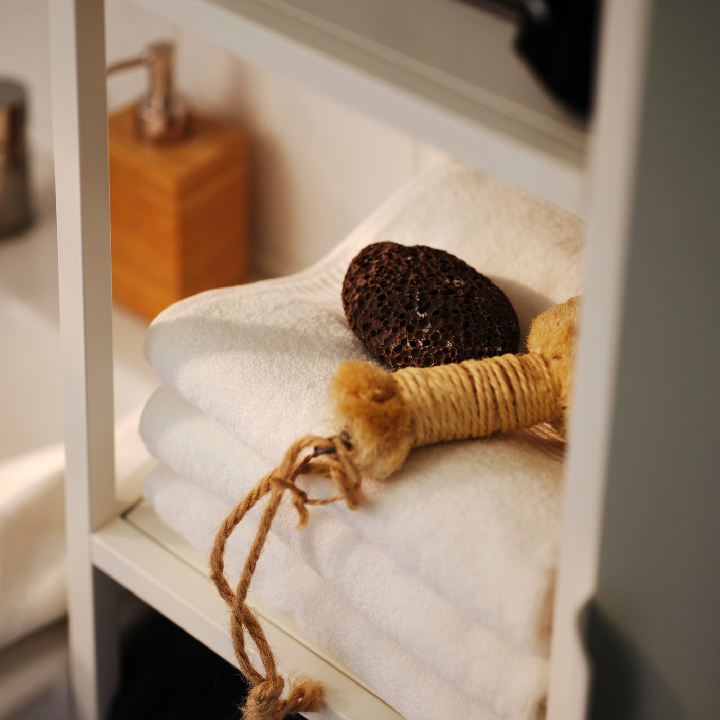 Tři bílé ručníky FREDRIKSJÖN na bílé otevřené polici vedle dávkovače na mýdlo.