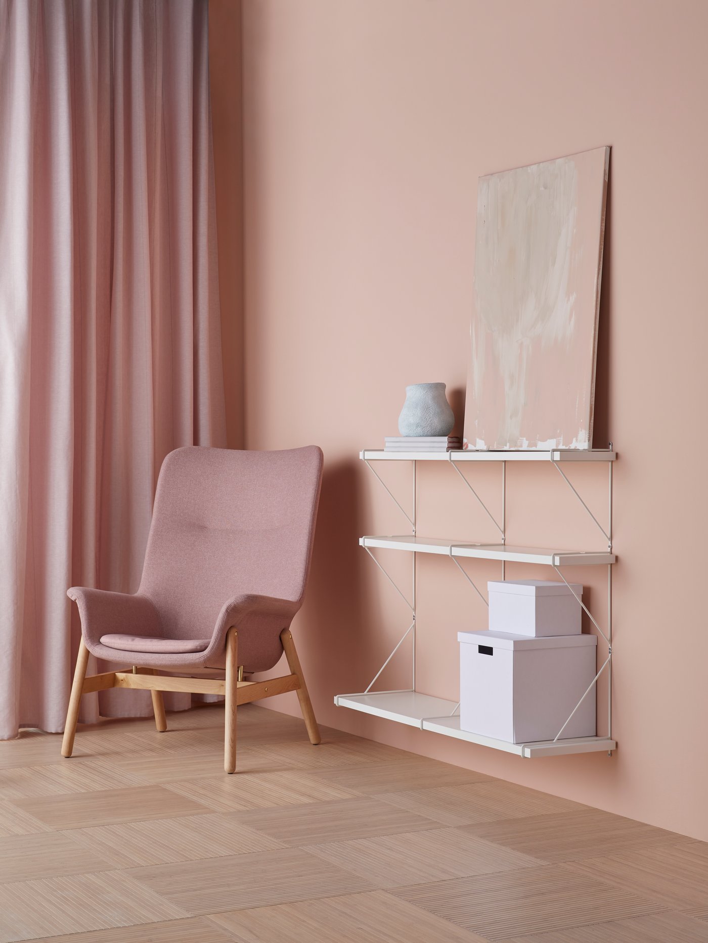 Salón con paredes y cortinas de color crema, un sillón de respaldo alto y un estante de pared con cajas y cuadros.