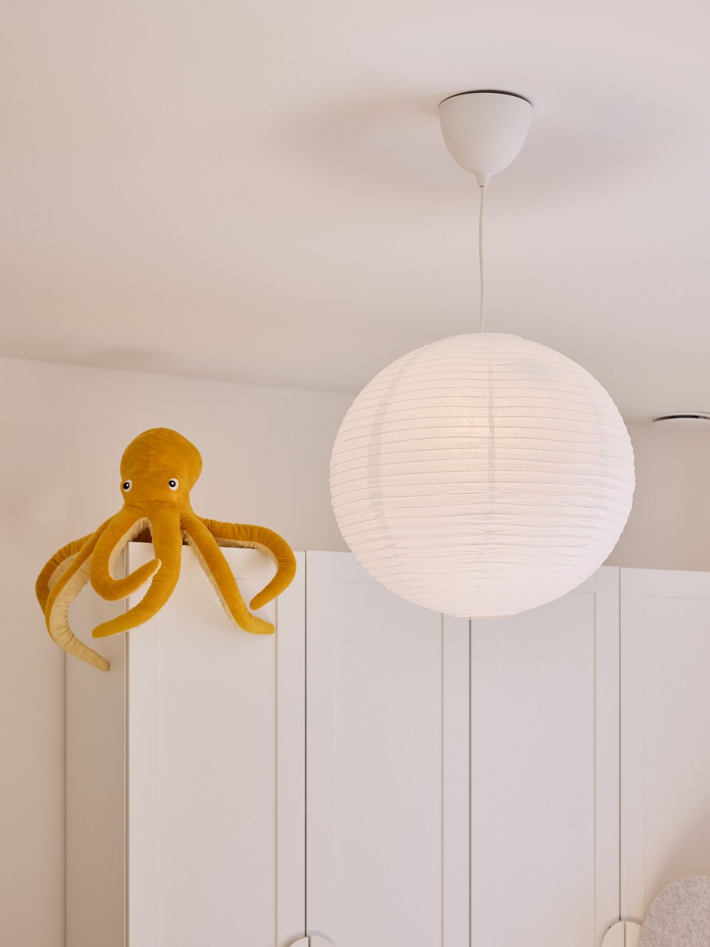 Pluchen octopus op witte kast naast ronde hanglamp, zachte kleuren en minimalistische kinderkamer.
