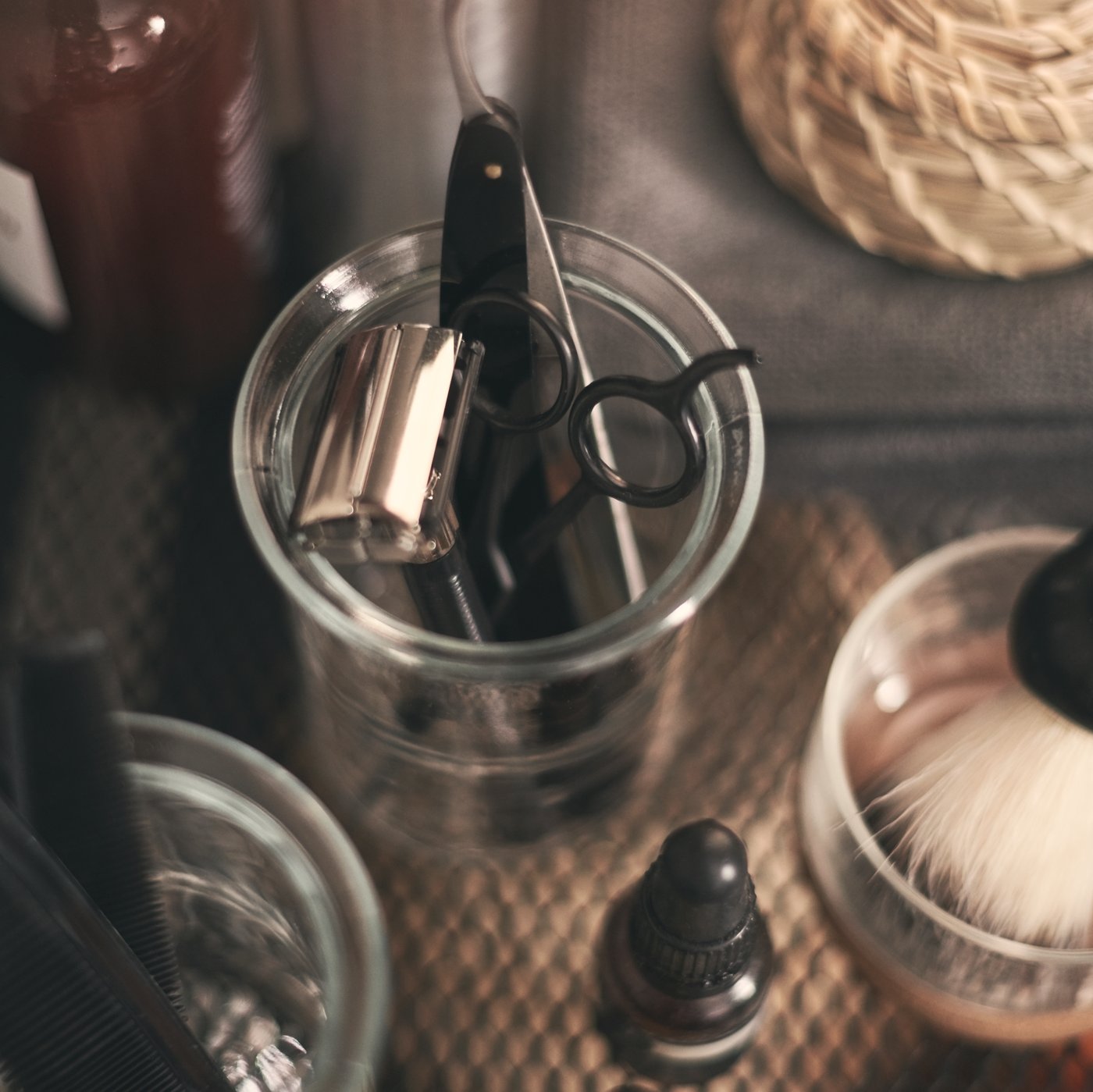 A VOXNAN glass mug holding scissors and razors, surrounded by other glass mugs holding bathroom accessories.