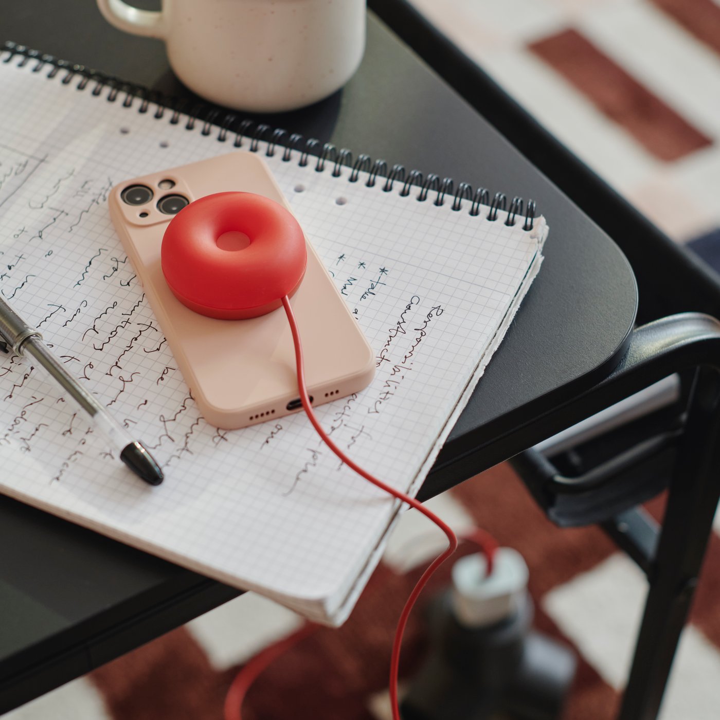 A round VÄSTMÄRKE wireless charger charges a mobile phone lying on a notebook on an OLSERÖD side table.