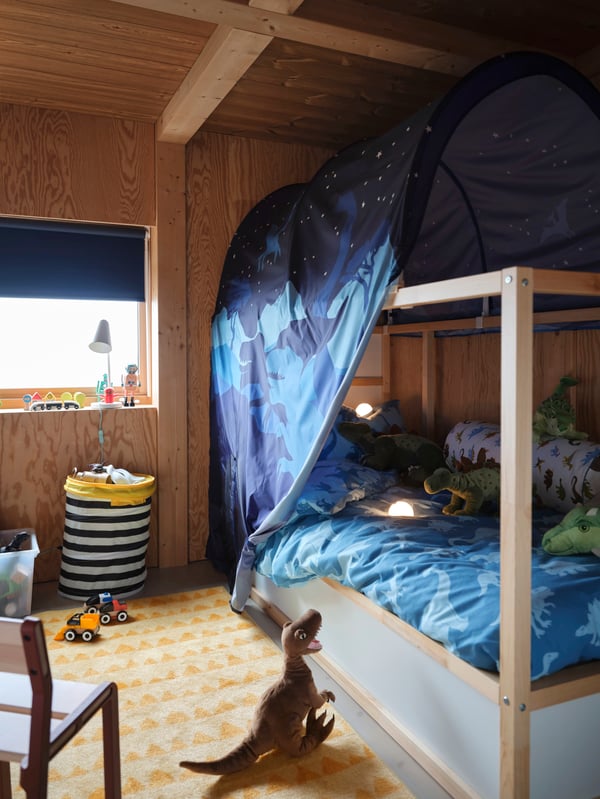 Two white extendable beds, a HÖVLIG children’s tent on a multicolour rug and a partially drawn white block-out roller blind.