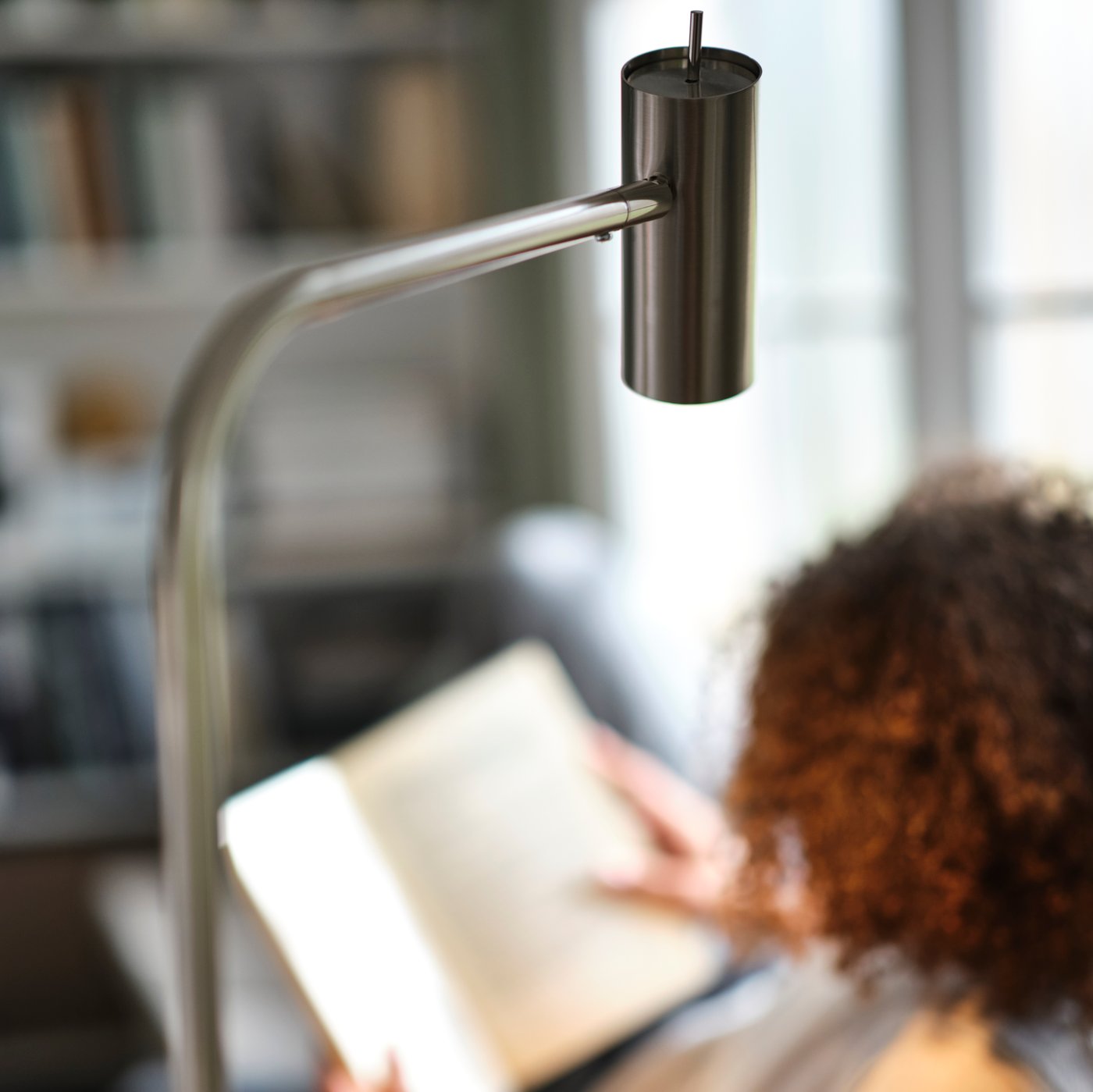 A close-up of the head and neck of a nickel-plated VIRRMO floor/reading lamp with a person reading under it.