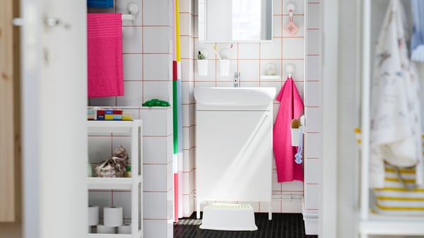 A bathroom with a colourful towels, a striped shower curtain, and a step stool, with toys and storage shelves nearby.