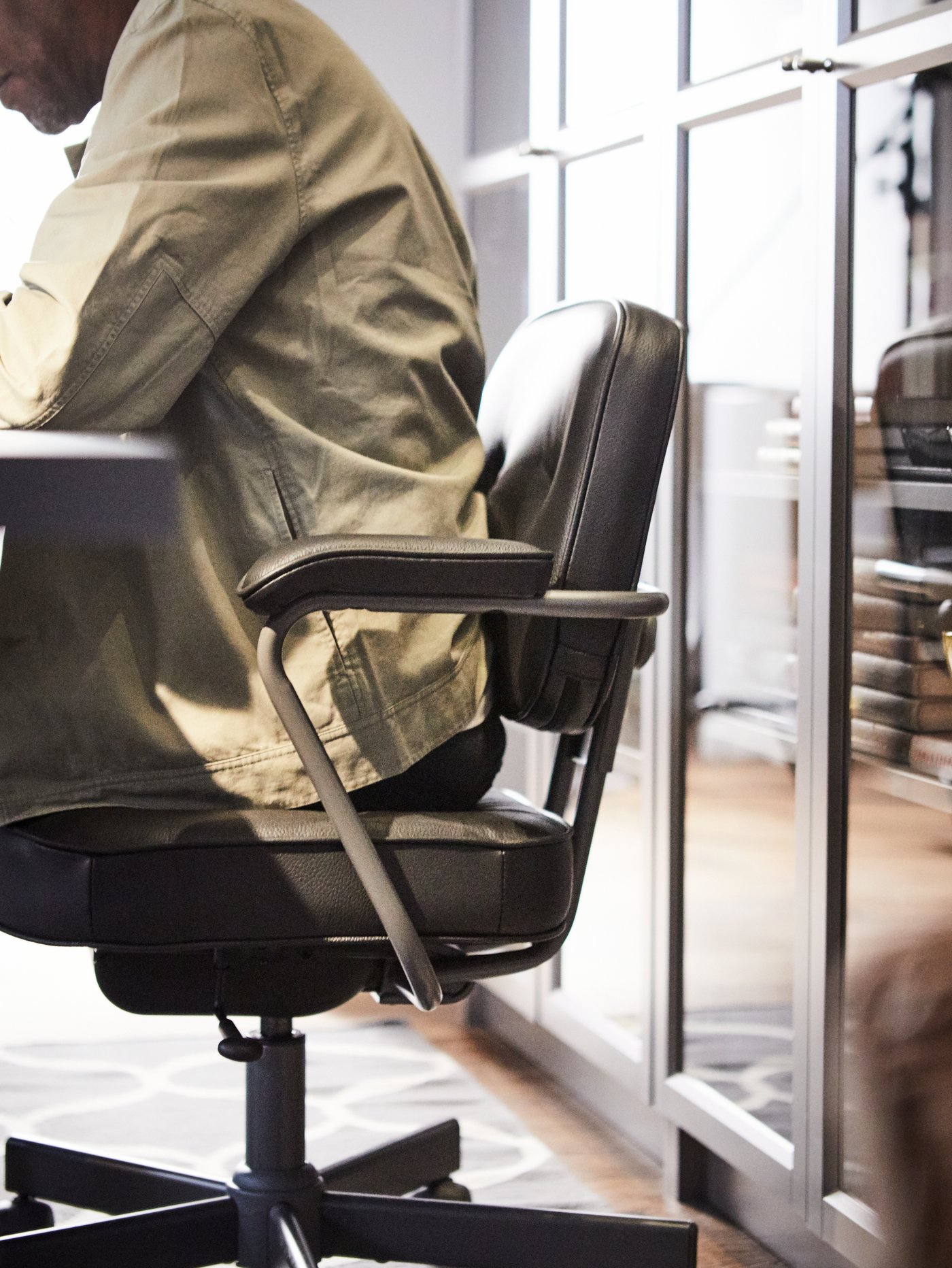 رجل يجلس على كرسي مكتب ALEFJÄLL أمام مكتبة BILLY.