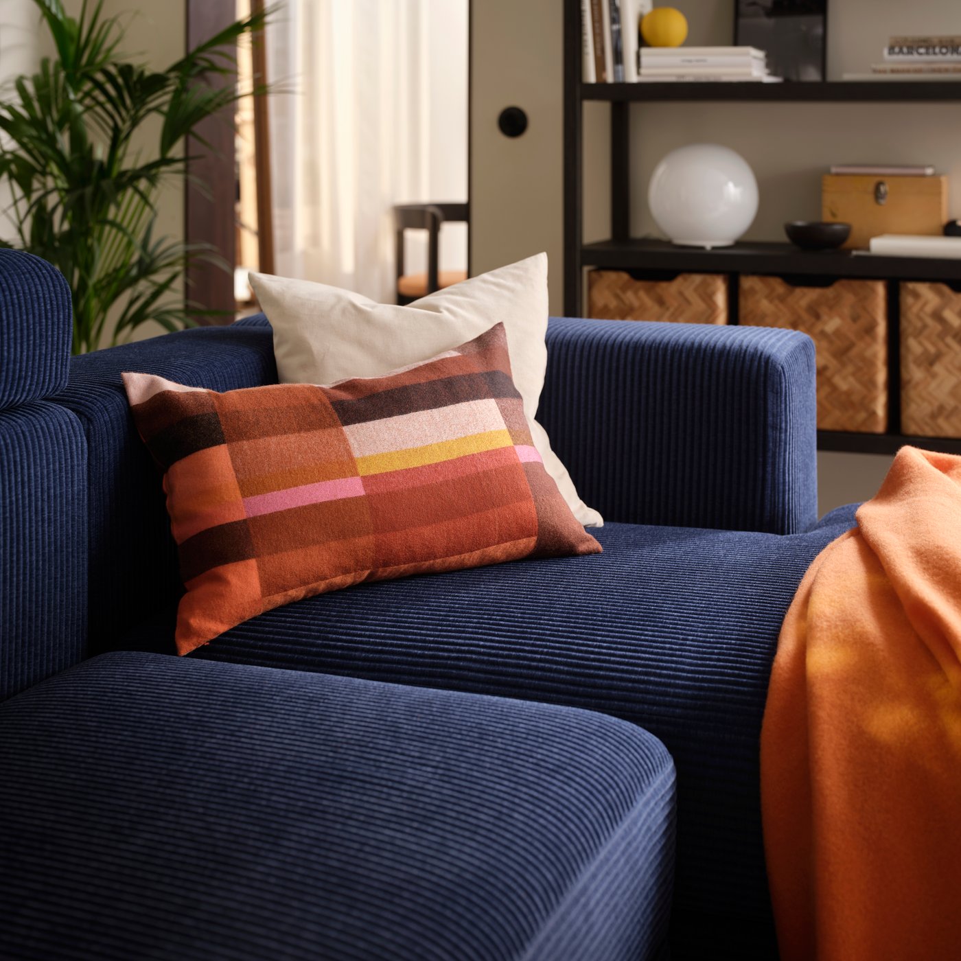 A living room with a dark-blue JÄTTEBO four-seat modular sofa with a chaise longue, holding a pair of cushions and a throw.