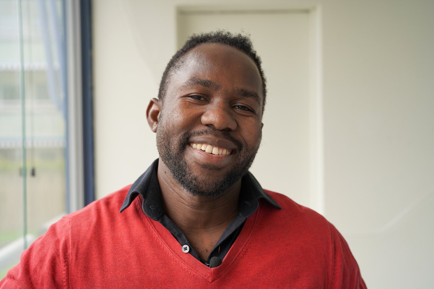 A man standing on a balcony in a red shirt looking towards the camera smiling.