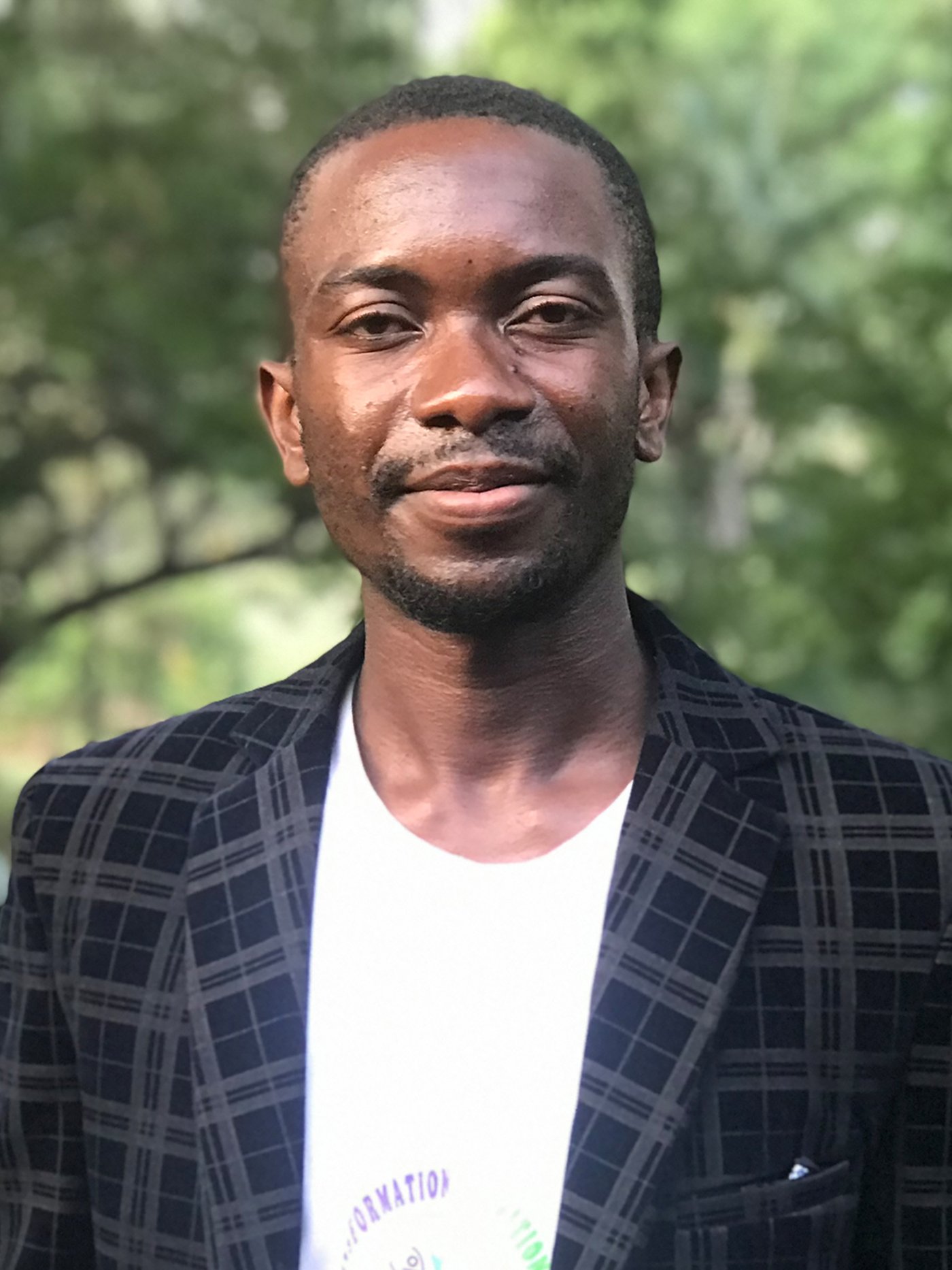 Portrait of Barthelemy, a Congolese reufgee, smiling at the camera wearing a dark blazer and white shirt.