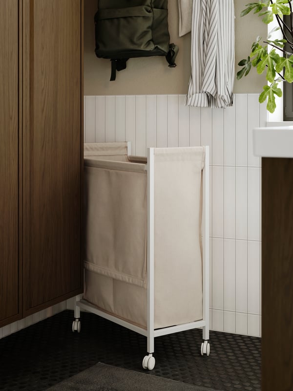 En beige tvättkorg står intill ett badrumsskåp i mörkt trä.