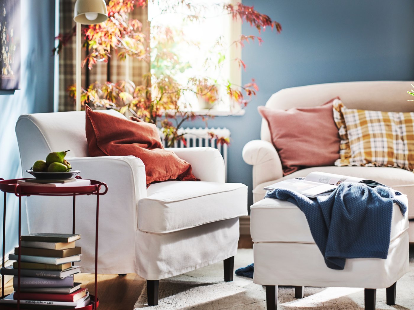 Ein weisser ROCKSJÖN Sessel und ein weisser ROCKSJÖN Hocker stehen in einem hellen Wohnzimmer neben einem ESSEBODA Sofa in Hellbeige.