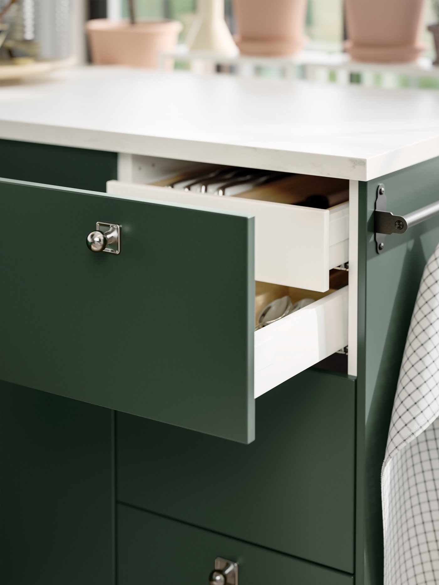 An open drawer in a kitchen with deep green HAVSTORP kitchen fronts and an inner drawer, both holding various items.