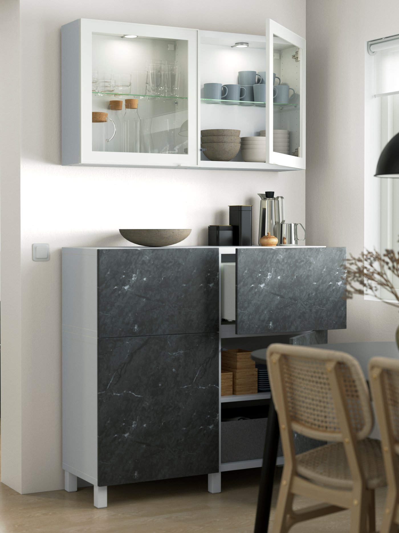 Dans un coin salle à manger, un meuble de rangment BESTA avec des portes BERGSVIKEN effet marbre entre ouverts, laissant apercevoir l'intérieur du placard.