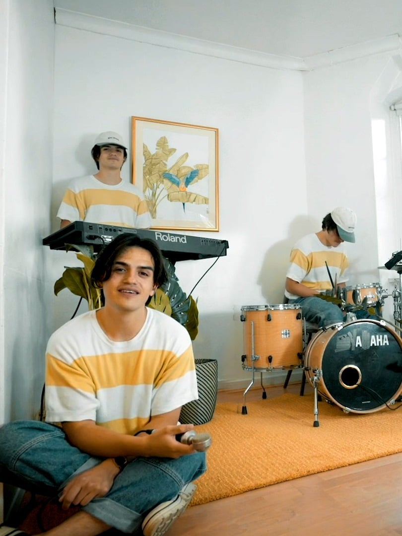 Tri člana benda spremaju se za svirku u prostoriji belih zidova.