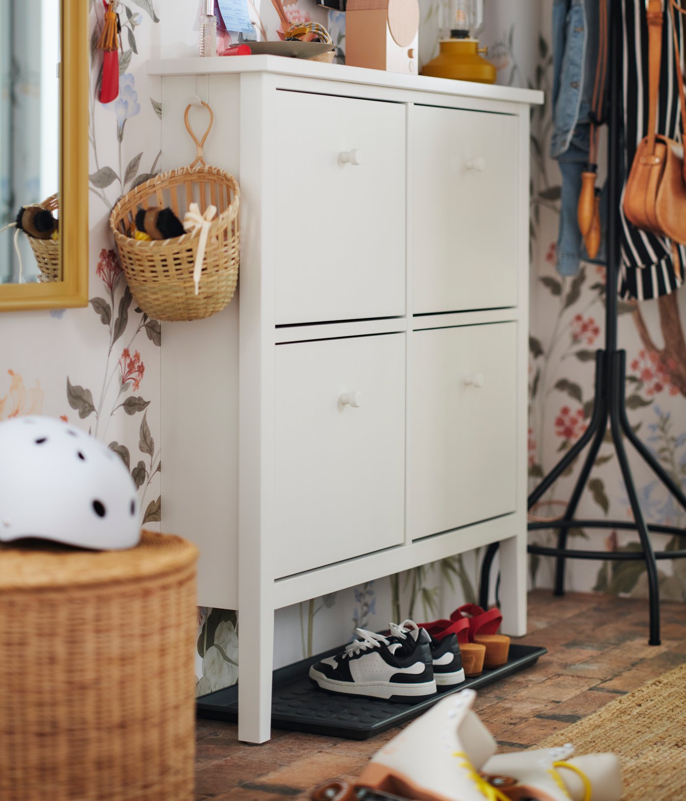 A white GULLABERG shoe cabinet against a floral wall with a basket hanging on one side and a BAGGMUCK shoe tray underneath.